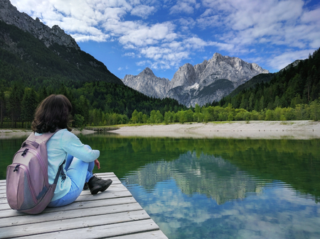 View of the Julian Alps from Kranjska Gora with Jasna Lake and girl sitting on pier in Sloveniaの写真素材