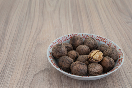 Whole walnuts and walnut kernels in white plate on wooden tableの写真素材