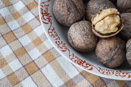 Whole walnuts and walnut kernels in white plate on table with checkered tablecloth