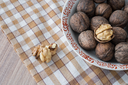 Whole walnuts and walnut kernels in white plate on table with checkered tableclothの写真素材