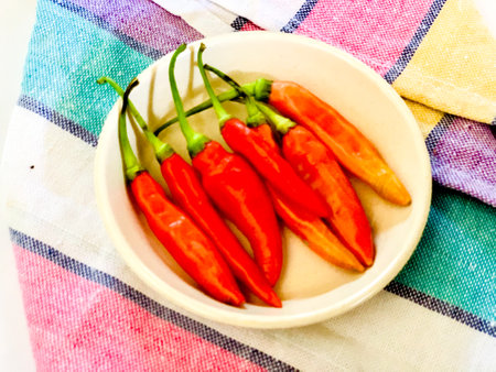Red hot chili peppers in a white bowl on a colorful tableclothの写真素材