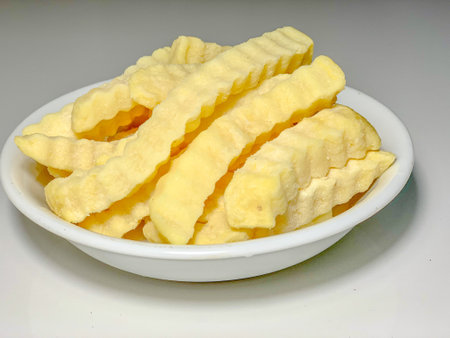 Crispy potato chips in white bowl on the grey background.