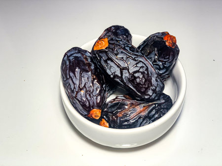 Dried dates fruit in a white bowl on a white background.