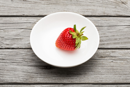 Fresh ripe strawberry in a simple white bowl, on gray wooden tableの写真素材