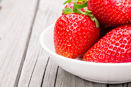 Fresh ripe strawberries in a simple white bowl, on gray wooden tableの写真素材