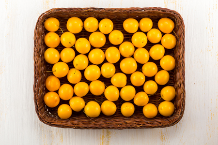 Yellow cherry plums in basket - on white wooden surfaceの写真素材