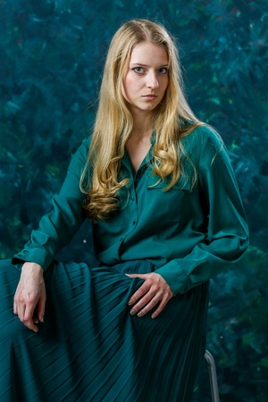 Beautiful Russian blonde girl on a green background in a long green dressの写真素材