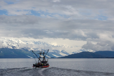 A salmon fishing boat is highlighted against the College Glaciers in Prince William Sound の写真素材