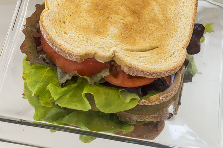 A classic BLT sits on a glass plate on a mirrorの写真素材