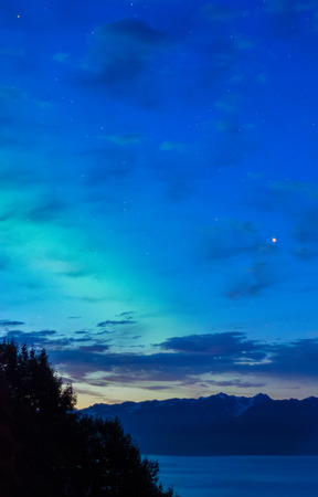 A band of green aurora wars with the coming dawn to be seen over Kackemak Bay on Alaska's Keanii Peninsula.の写真素材