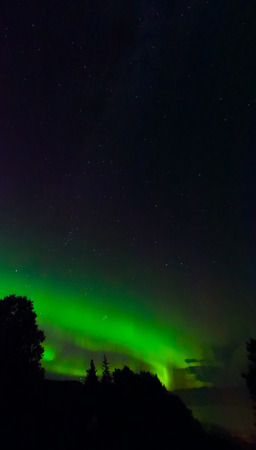 Dual bands of green aurora peek over a ridge under an almost cloudless night.の写真素材