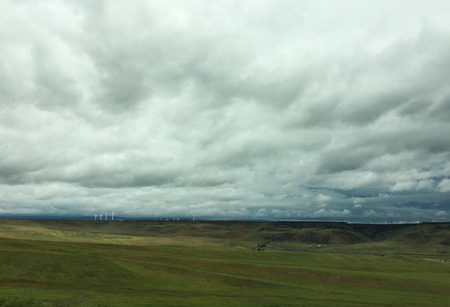 Wind mills turn in the distance under rolling white cloudsの写真素材