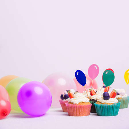Happy Birthday day cupcake and cake bakery with candles, bright lights bokeh. Background holiday with confetti, balloon and place for text.の写真素材
