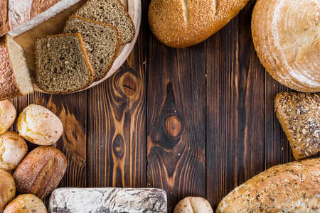 Different baking buns, croissants, gingerbread cookies. Delicious freshly baked bread on wooden background with place for text. Fresh loaves of bread And sliced ââbreads containing sesame seeds.の写真素材