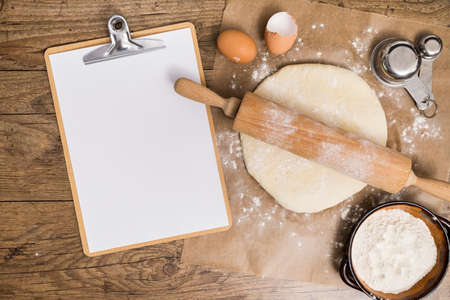 Flour and kitchen utensils whisk, baking dish, rolling pin with eggs on the table. Baking, cooking concept, top view with place for text.の写真素材