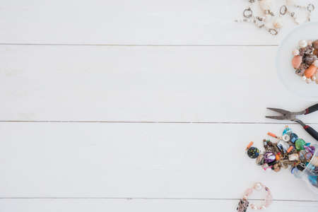 Box with beads, spool of thread, plier and glass to create hand made jewelry on wooden background with place for text. Top viewの写真素材