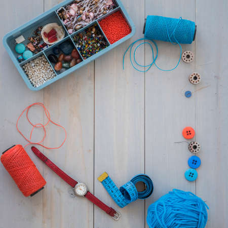 Box with beads, spool of thread, plier and glass to create hand made jewelry on wooden background with place for text. Top viewの写真素材