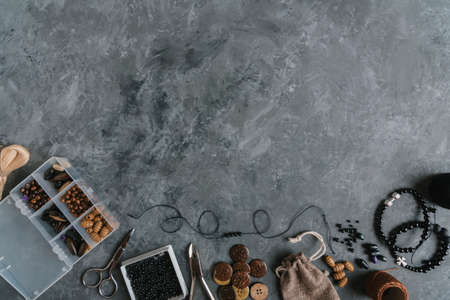 Box with beads, spool of thread, plier and glass to create hand made jewelry on wooden background with place for text. Top viewの写真素材