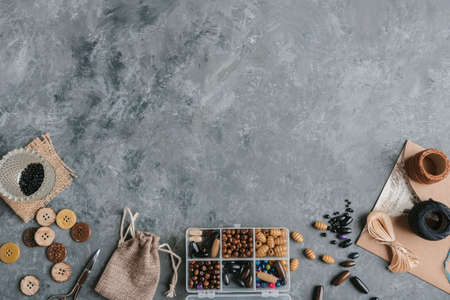 Box with beads, spool of thread, plier and glass to create hand made jewelry on wooden background with place for text. Top viewの写真素材