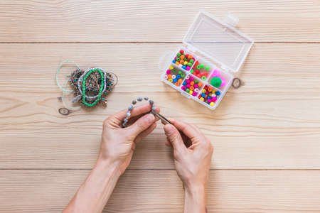 Making of handmade jewelery. Box with beads on old wooden table. Top view with woman hands. Beads...