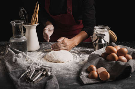 Beat flour and kitchen utensils, a baking dish, a rolling pin with eggs on the table. Baking, cooking concept. Chef making bread and gingerbread cookies. The cook kneads and rolls the dough.の写真素材