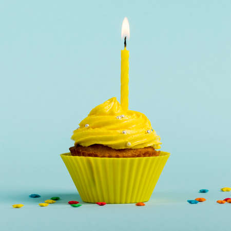 Yellow burning candles decorative muffins with colorful star sprinkles against blue backdrop. High quality photoの写真素材