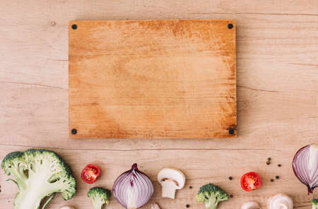 Wooden chopping board with broccoli tomatoes onion mushroom black pepper table. High quality photo
