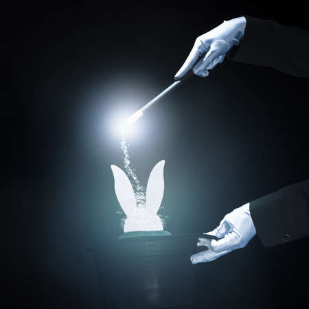 magician performing trick with magic wand against black glowing background. Resolution and high quality beautiful photoの写真素材