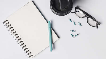 blank spiral notepad pen coffee cup eyeglasses pushpins white background. High quality beautiful photo conceptの写真素材
