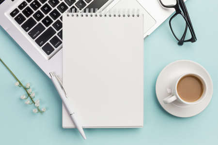pen spiral notepad laptop with eyeglasses flower twig coffee cup blue office desk. High quality beautiful photo conceptの写真素材