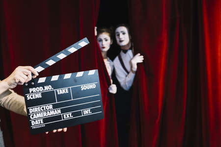 person holding clapperboard front mime couple standing red curtain. High quality beautiful photo...