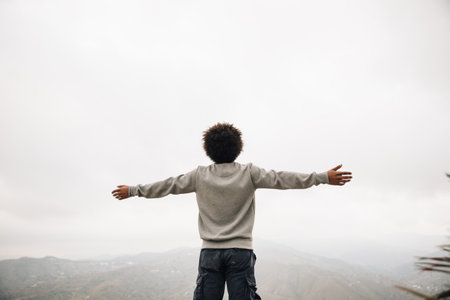 rear view african young man standing top mountain outstretching his hand.の写真素材