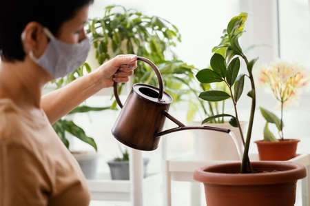 side view woman with face mask using watering can indoor plant. High quality photoの写真素材