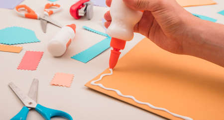 human hand applying white glue orange paper with scissor staplerの写真素材