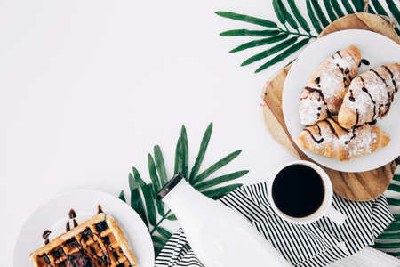 overhead view baked croissant waffles bottle coffee cup leaves white backdropの写真素材