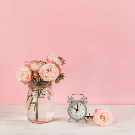 roses vase near alarm clock wooden desk against pink background. High quality photo