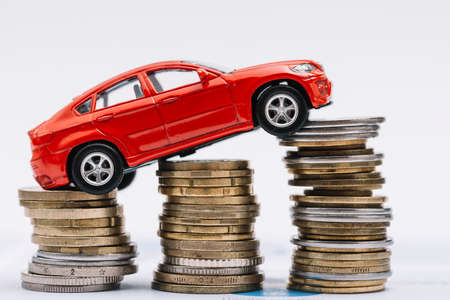 toy red car stack increasing coins against white backgroundの写真素材