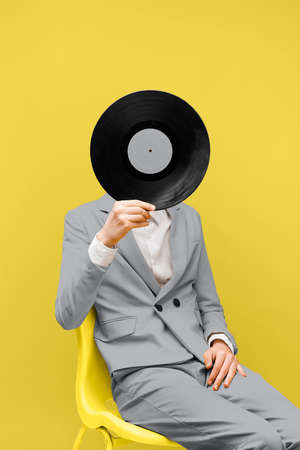 man covering his face with vinyl record while wearing ultimate gray clothes. High quality photoの写真素材