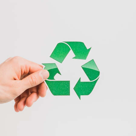 person s hand holding green recycle symbol white backdrop. High quality photoの写真素材