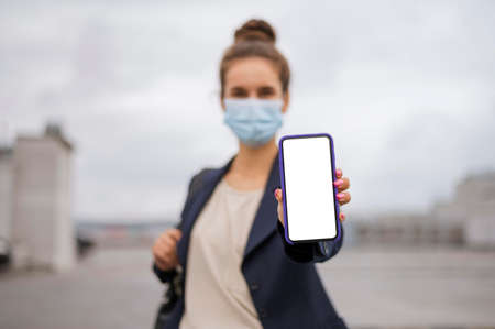 businesswoman holding blank smartphone while wearing medical mask. High quality photoの写真素材
