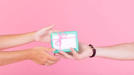man s hand giving gift her woman against pink background. High quality photoの写真素材