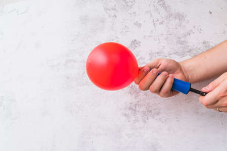 close up hand blowing red balloon with pump against wall. High quality photoの写真素材