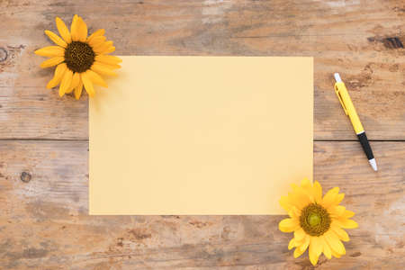 elevated view blank paper with yellow sunflowers pen wooden backdrop. High quality photoの写真素材