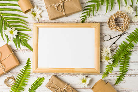 elevated view blank frame surrounded by gifts leaves white flowers. High quality photoの写真素材