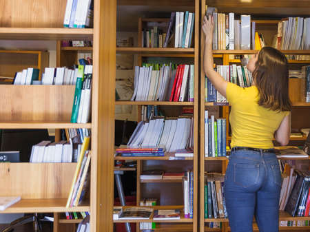 teen girl taking book from top bookcase. High quality photoの写真素材