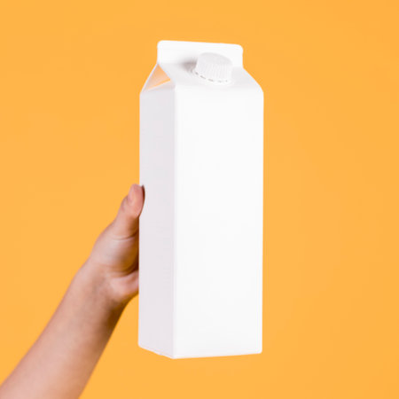 human hand holding white carton yellow background. High quality photoの写真素材