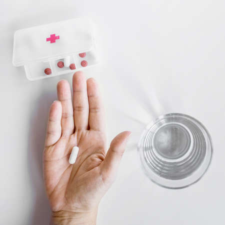 person s hand taking tablet from pill organizer box white background. High quality photoの写真素材