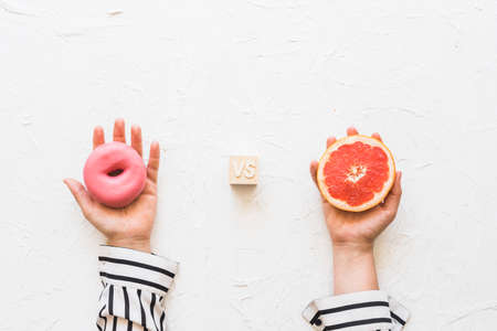woman s hand holding pink donut versus grapefruit slice textured backdrop. High quality photoの写真素材