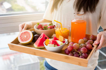 smiling young woman standing against window holding tray fruits juice. High quality photoの写真素材