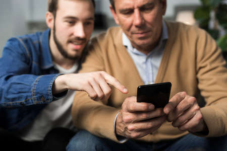 father son looking phone living room. High quality photo